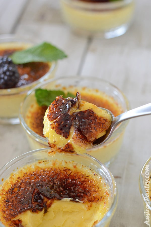 A spoon holding some easy creme brulee with craked caramelized sugar in focus with other ramekins in the background.