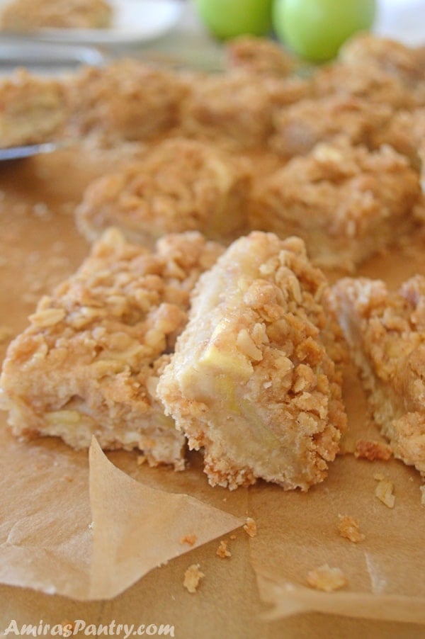 Apple crisp bars scattered on parchment paper with green apples in the back.