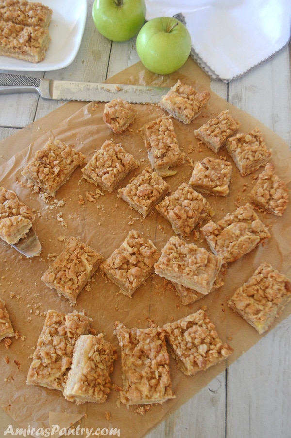 Apple crisp bars scattered on parchment paper with green apples in the back.