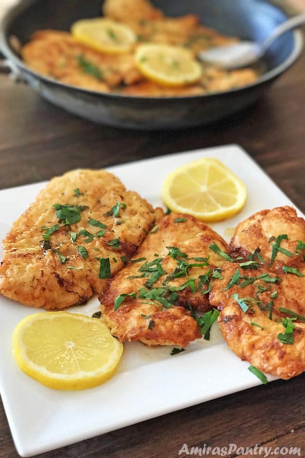 Three pieces of Chicken Francese on a white plate with lemon rinds.