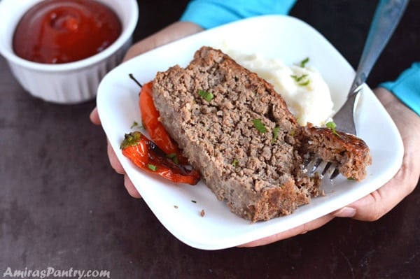 Hands holding a plate with slices of moist beef meatloaf