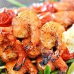 A plate of grilled shrimps on skewers with two shrimps in focus.