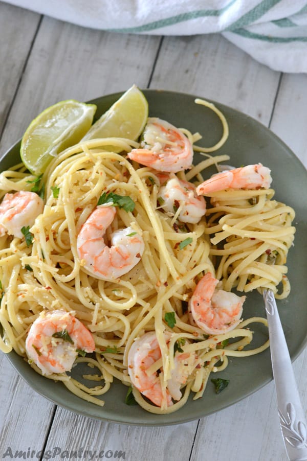 A plate with shrimp scampi linguine with lemon wedges and fork on the plate.