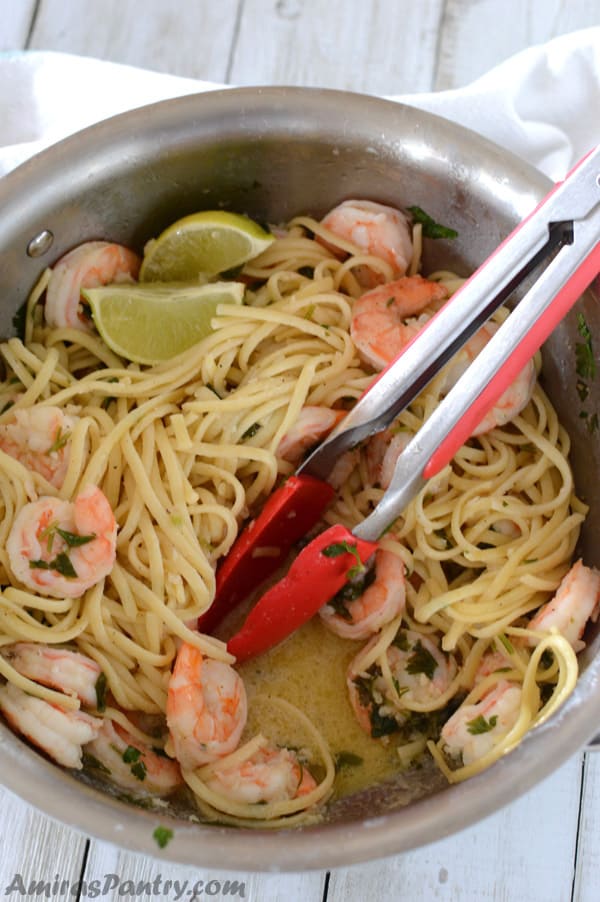 A pot full of shrimp scampi with tonges in it showing the sauce.