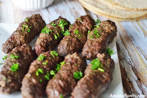 kofta arranged on a white plate with pita bread on the back.