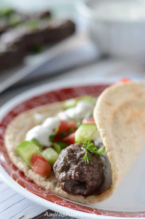 A kofta finger wrapped in pita bread and topped with salad and tzatziki sauce