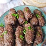 A green serving plate with Kofta fingers and pita bread on the back.