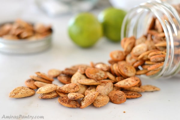 A jar full of shawarma roasted pumpkin seeds tilted to its side with some seeds falling out of it