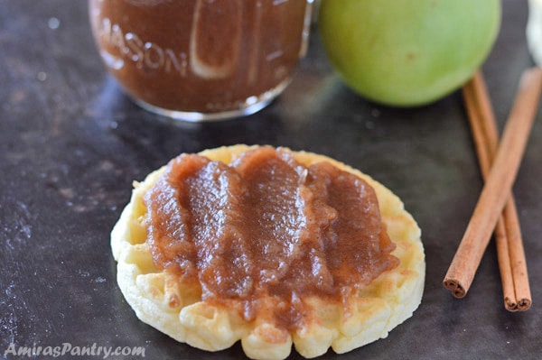 A waffle spread with thick apple butter with cinnamon sticks on the side.