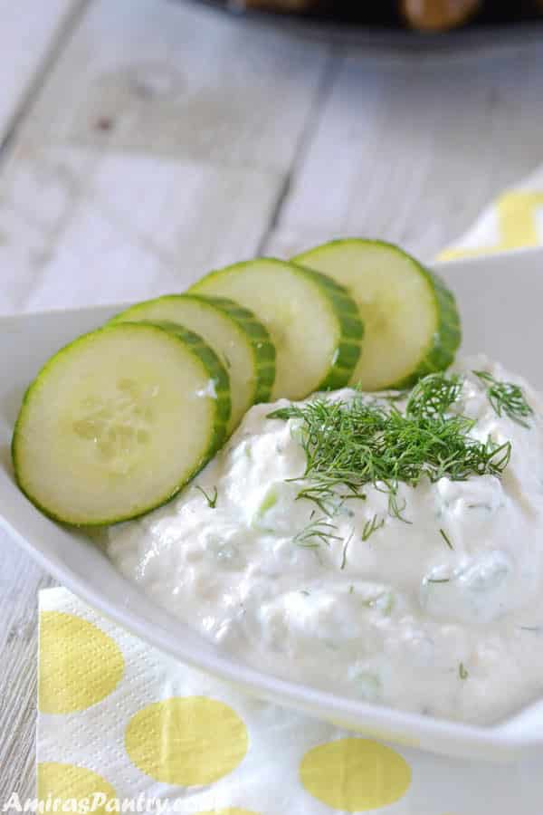 A white triangular shaped plate with tzatziki sauce and some cucumber rings on the side
