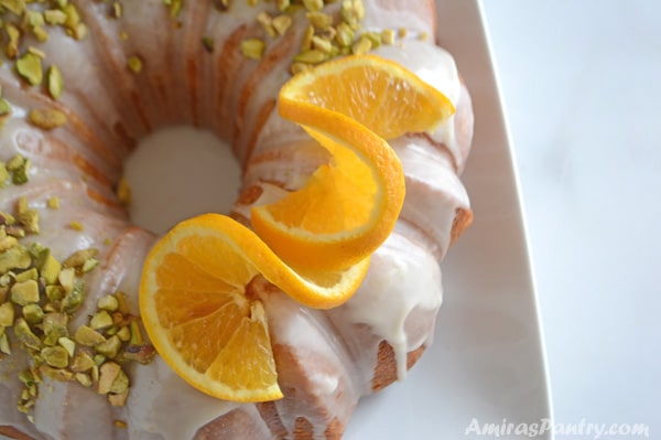Golden saffron orange bundt cake with orange slices on top and sprinkled with pistachios