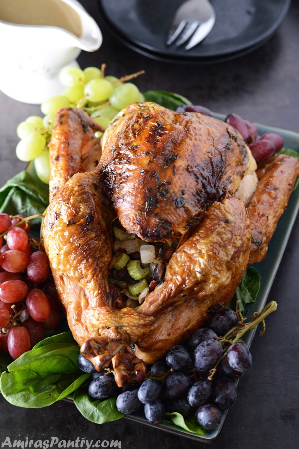 Perfectly roasted and moist turkey on a serving platter surrounded by grapes with gravy in the back