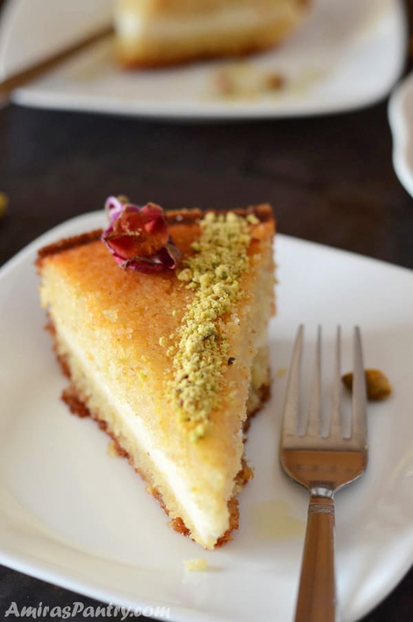 A wedge of semolina cake with cream served on a white plate with a fork next to it