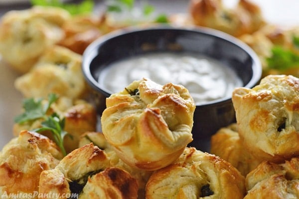 Spanakopita with puff pastry in a pile with a plate of tzatziki sauce at the back.