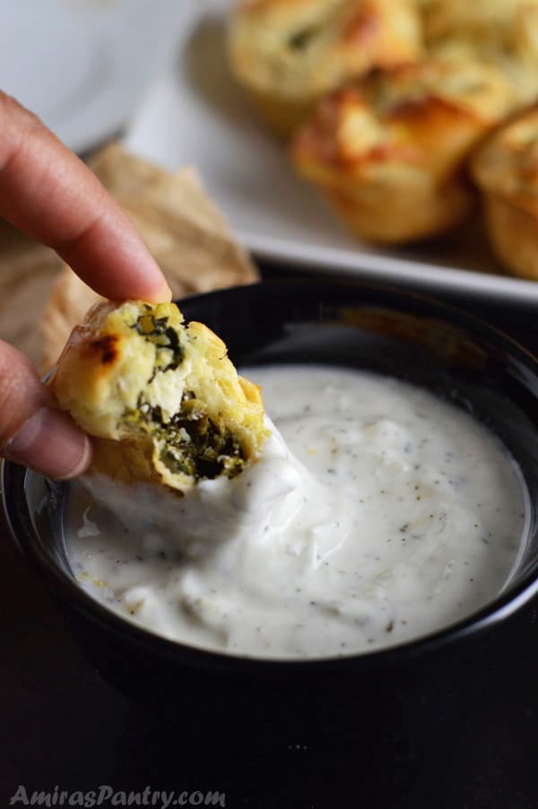 Hand dipping a spanakopita puff in tzatziki sauce.