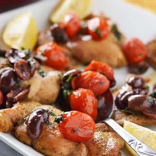 A plate of food, with Chicken, olives and tomatoes