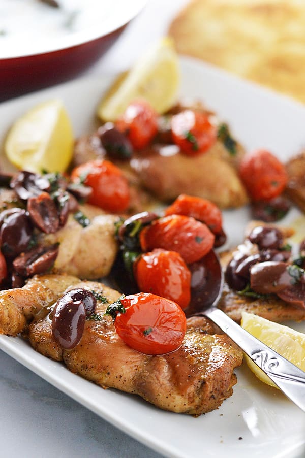 A plate of food, with Chicken, olives and tomatoes