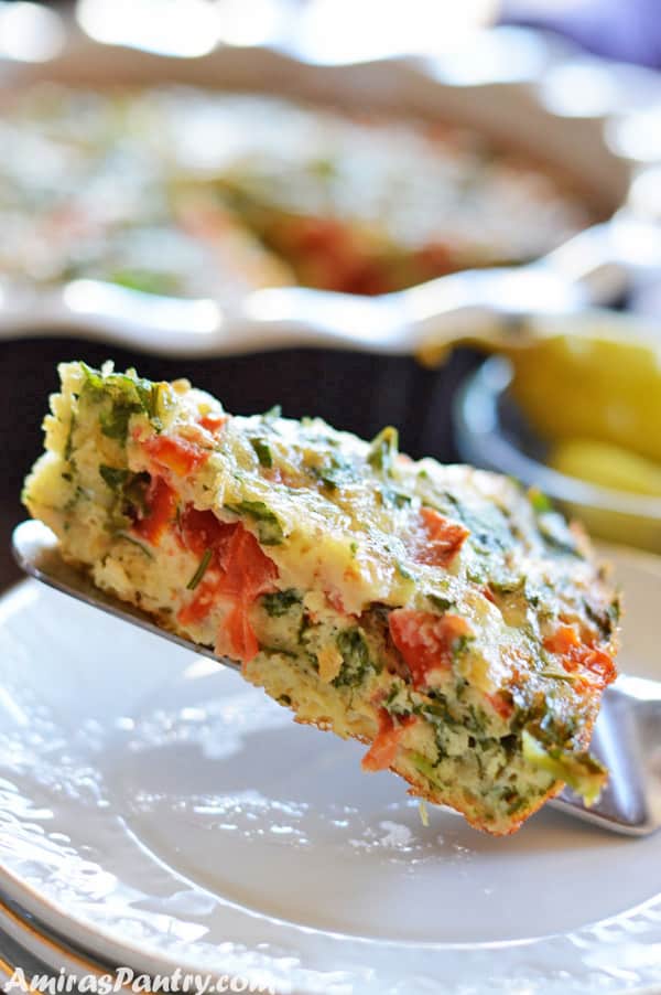 A serving spoon with a wedge of frittata on it with the whole pan on the back.