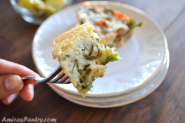 A hand holding a fork with a piece of breakfast frittata in it.