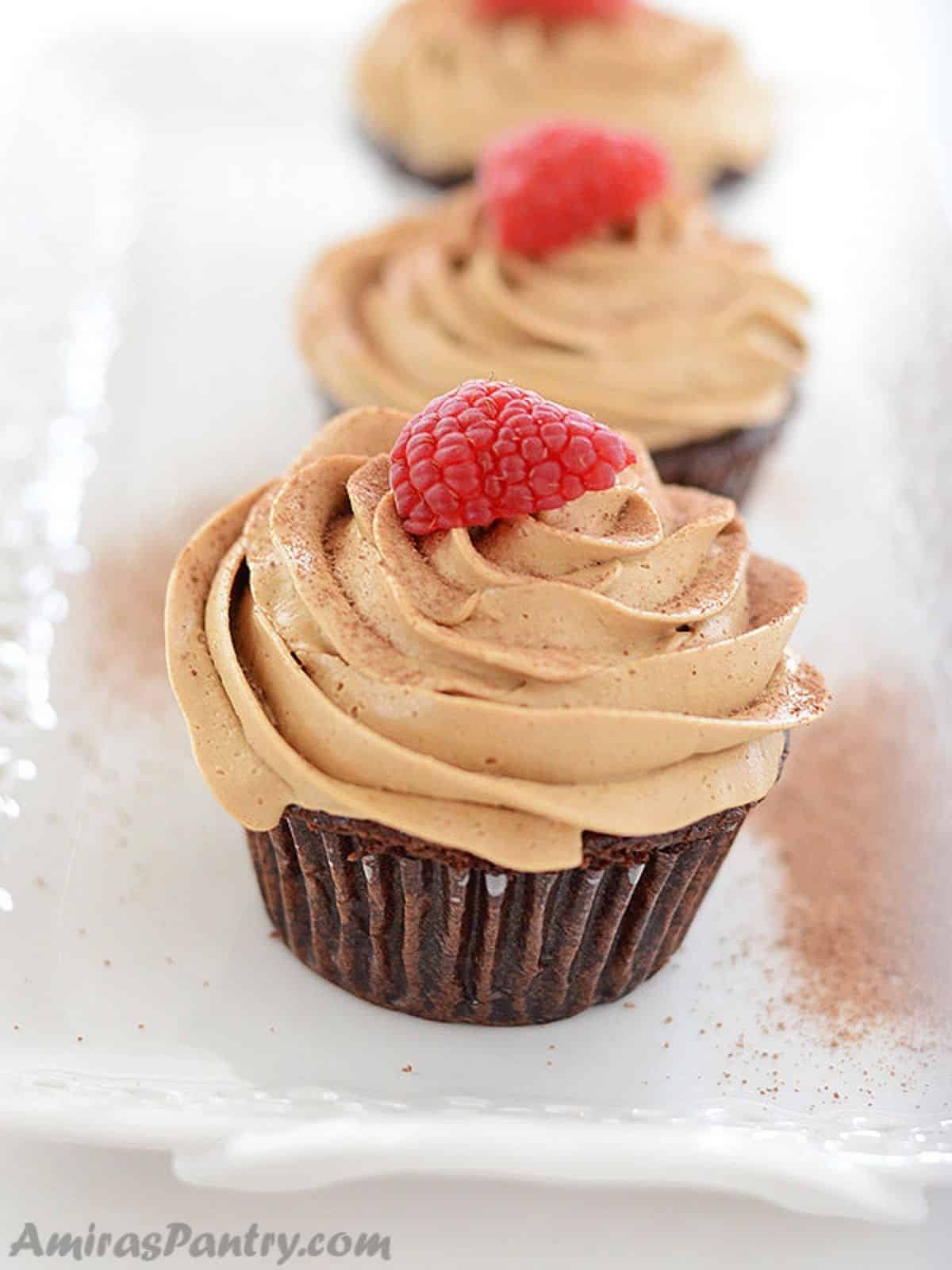Coffee cupcakes placed on a white serving platter topped with raspberries.