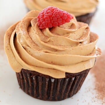 A close up image to coffee cupcakes topped with raspberries.
