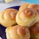 Sweet bread rolls stacked on a dark blue plate with a bottle of milk and a piece of butter in the back.