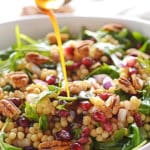 A bottle pouring dressing over mediterranean couscous salad