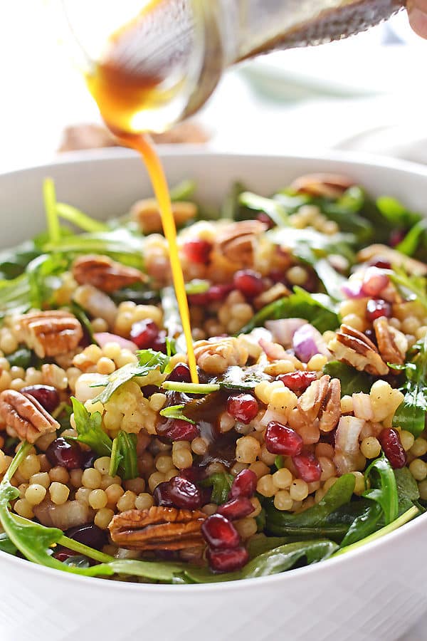 A bottle pouring dressing over mediterranean couscous salad