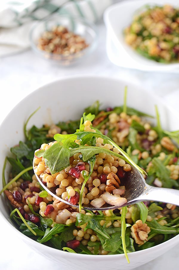 A spoon scooping some of the Mediterranean couscous salad with the whole bowl in the back.