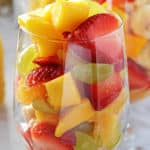 A glass filled with fruit salad to the brim with another one on tha back.