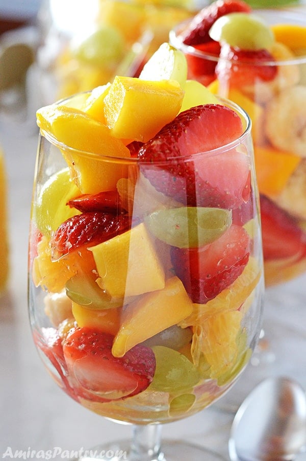A glass filled with fruit salad to the brim with another one on tha back.