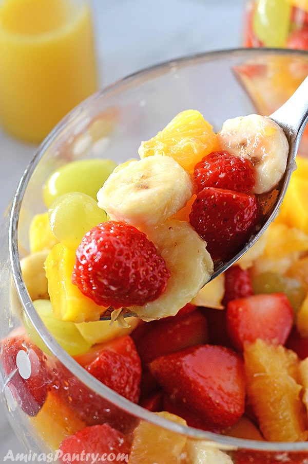 A spoon scooping some fruit salad from a bowl.