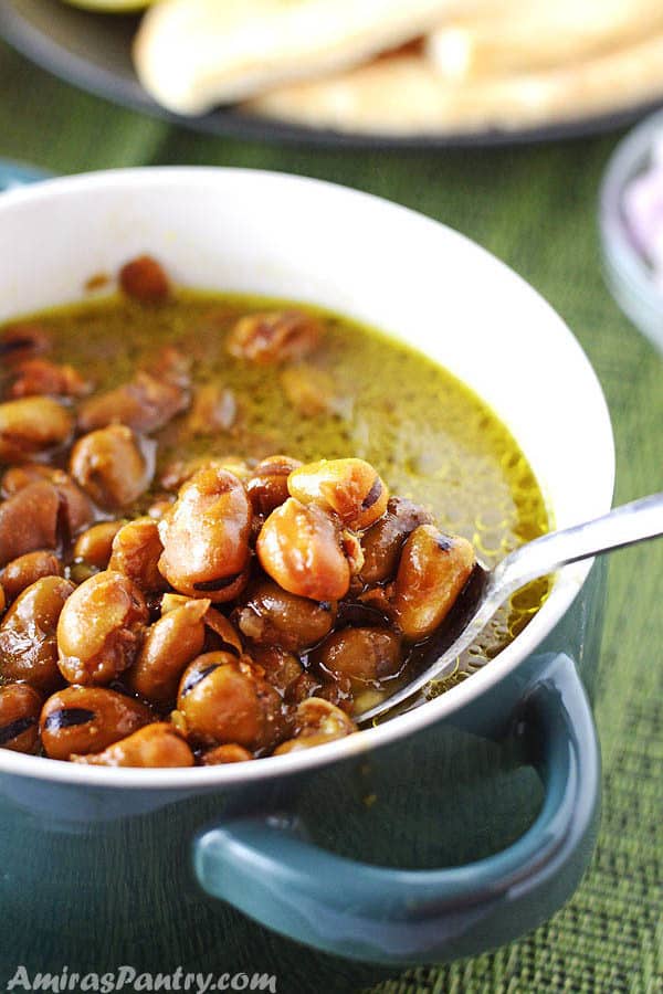 A bowl of ful, Egyptian fava beans, with a spoon scooping some of the beans out