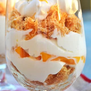 A close up of a glass cup filled with Knafeh and cream
