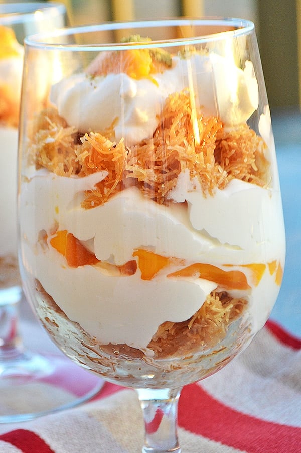 A close up of a glass cup filled with Knafeh and cream