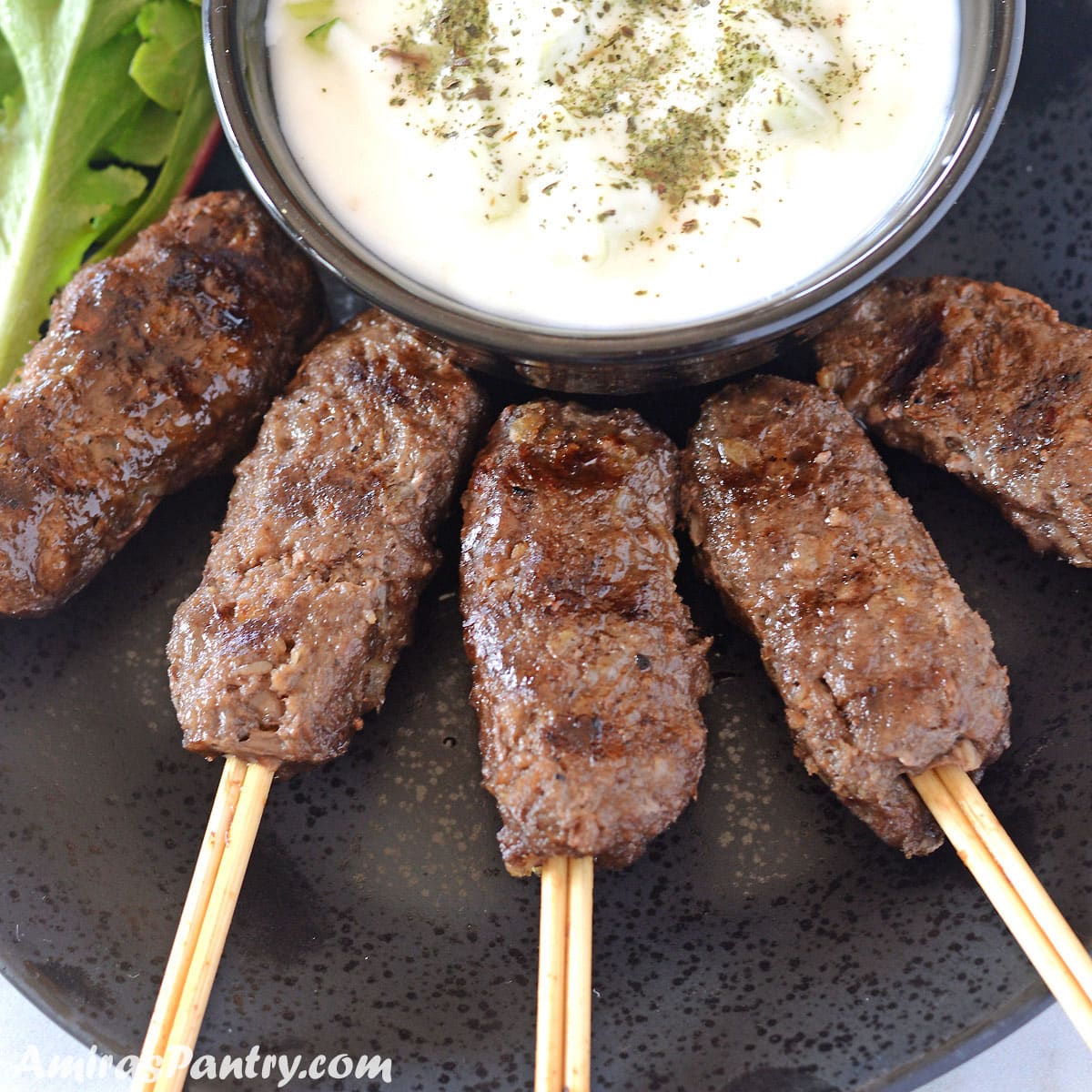 Kofta skewers on a black plate with a bowl of tzatziki sauce