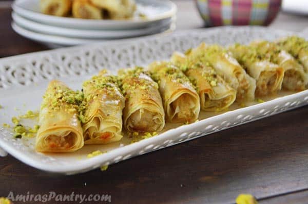 Baklava rolls on a white plate and sprinkled with crushed pistachios.