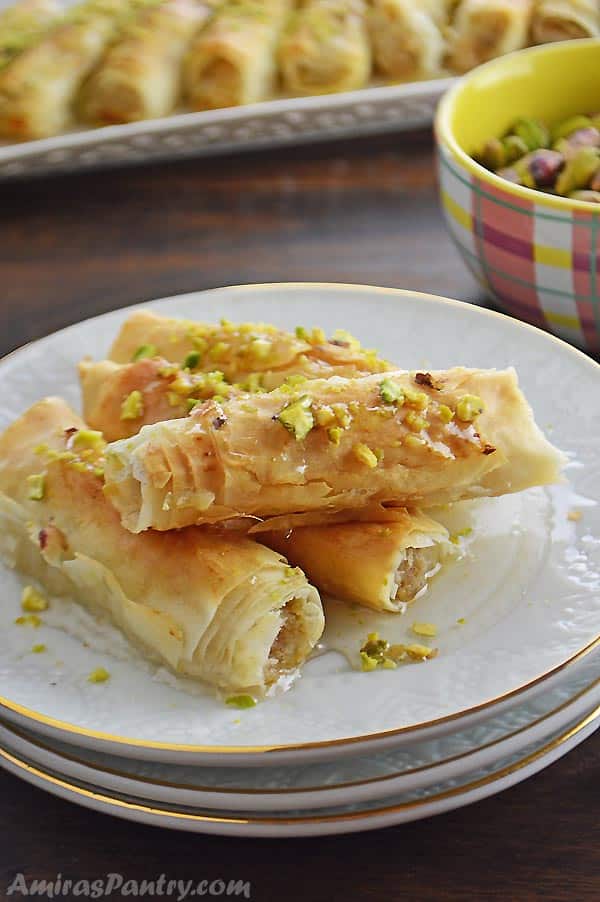 Phyllo rolls placed on a stack of white plates and sprinkled with pistachios.