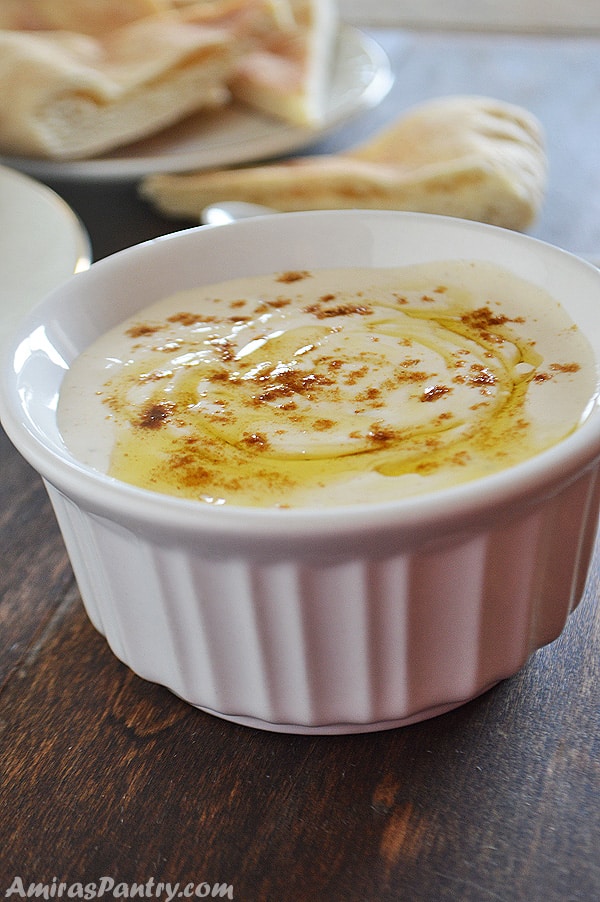 Tahini sauce in a white bowl with pita bread on the back.