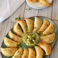 Beef empanadas on a big green platter with a bowl of guacamole in the middle