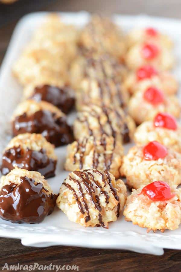 A white serving plate with coconut macaroons topped with cherries with some drizzled in chocolate.