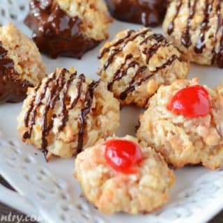 A white serving plate with coconut macaroons dipped in chocolate and a cherry on top.