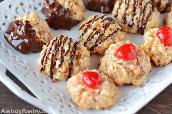 A white serving plate with coconut macaroons dipped in chocolate and a cherry on top.