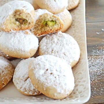 A white plate with kahk cookies dusted with powdered sugar with one open at the top.