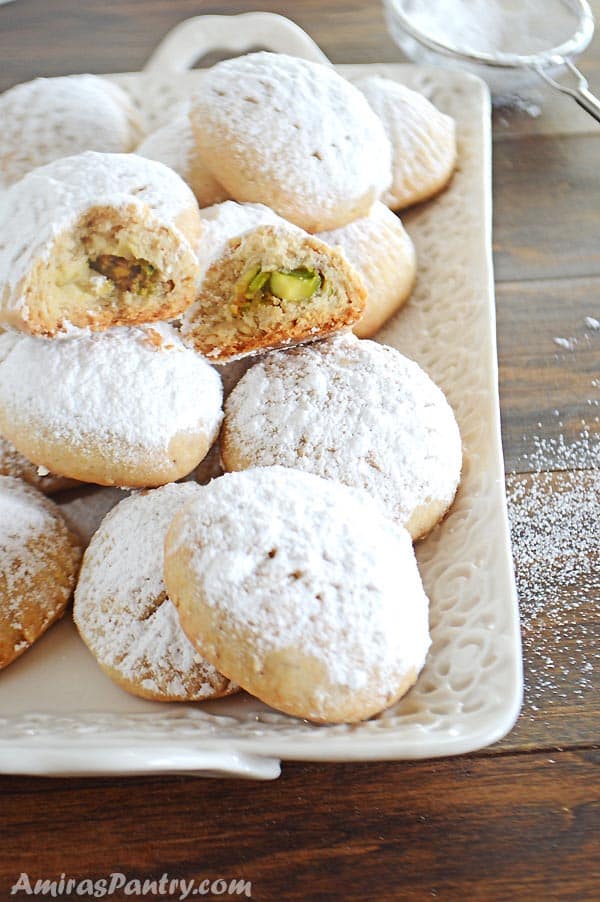 A white plate with kahk cookies dusted with powdered sugar with one open at the top.