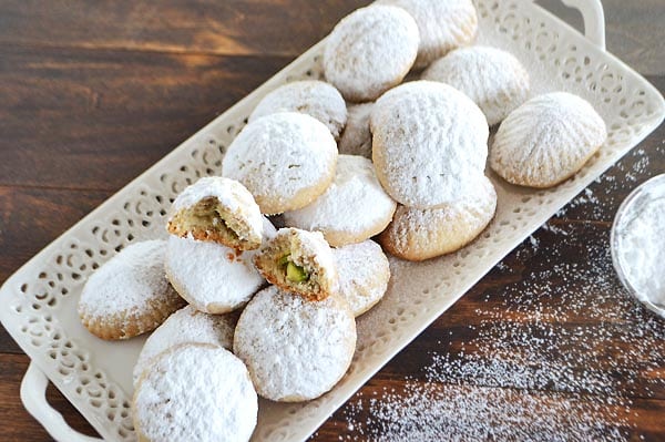 a white serving plate with kahk dusted with powdered sugar with some powdered sugar on the table.