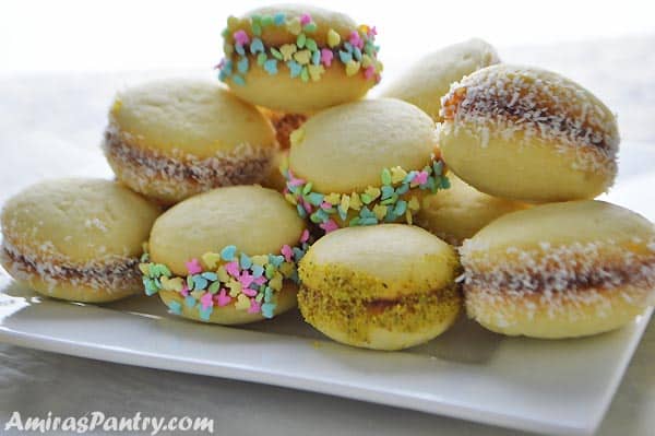 a white plate with a pile of lancashire cookies dipped with ground nuts and sprinkles.