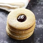 A stack of linzer cookies filled with jam with a white kitchen cloth in the back.