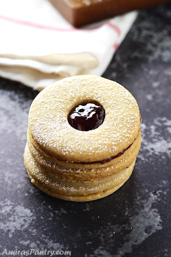 A stack of linzer cookies filled with jam with a white kitchen cloth in the back.