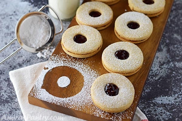 A wooden board with linzer cookies lined on it with one missing.
